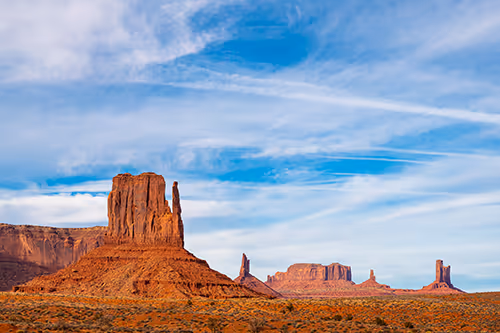 Red sandstone buttes in Monument Valley under a blue sky with wispy clouds.